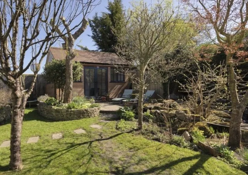 The studio seen from across the garden, surrounded by trees, planting and a stone path.