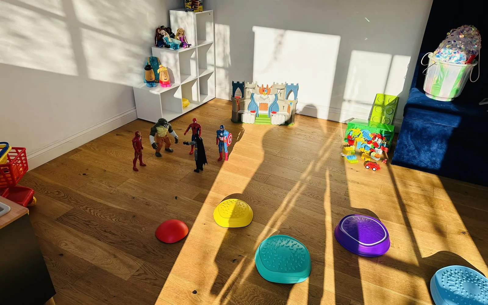 Sunlight across the studio floor with superhero figures, building blocks and sensory stepping stones set out for a therapy session.