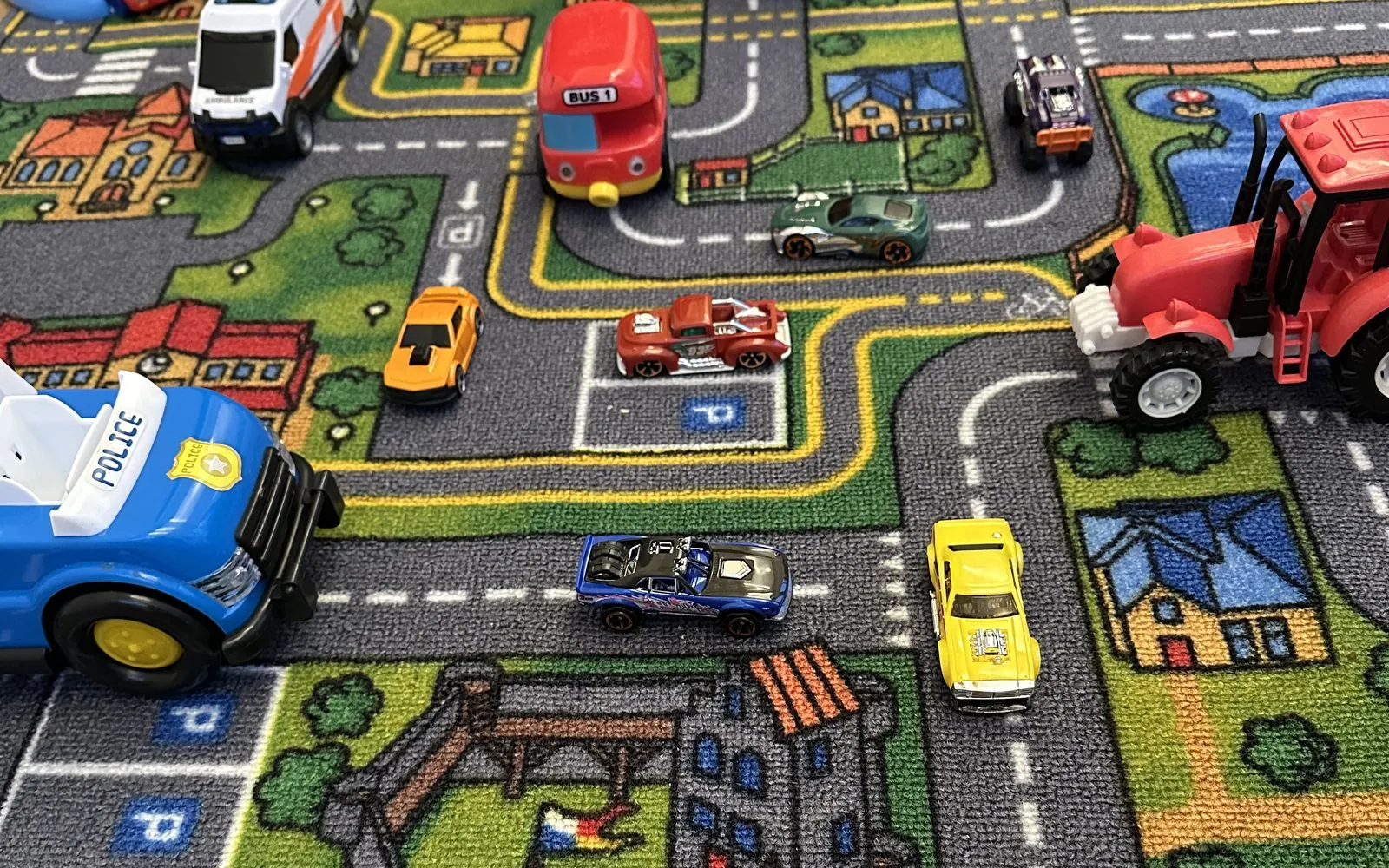 A road play mat with toy cars, a fire station and a tractor, used for motivating play-based speech and language therapy.